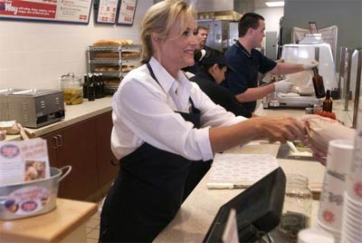 Dawn Robinson rings up sandwiches at the Jersey Mike's in Camarillo that she and husband Troy own. Below, Ryan Gerry cleans tables beneath a suitcase Robinson's uncle used to bring subs from the original Mike's Subs in New Jersey when she was a child. \"It might be why I still like the subs day-old,\" she says.

